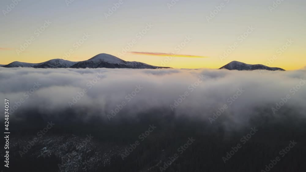 Aerial view of vibrant sunrise over white dense fog with distant dark peaks of Carpathian mountains on horizon.