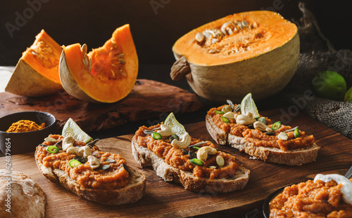 Toasted bread bruschetta with vegetable caviar made of squash pumpkin with green pepper, nuts, lime on wooden cutting board on dark background. Healthy vegan food, clean eating, close up