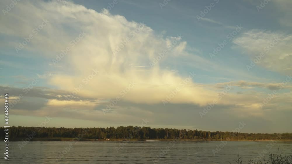 Large cumulus clouds in a panoramic view over the lake in the evening. The picturesque landscape of heaven above the water surface in the summer season. Recreation place with a water scooter rider. Large cumulus clouds in a panoramic view over the lake in the evening. The picturesque landscape of heaven above the water surface in the summer season. Recreation place with a water scooter rider.