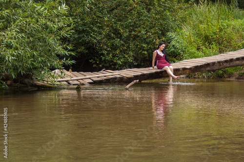 Girl sitting on a wooden bridge over the river and reading a book