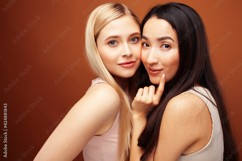 two pretty diverse girls happy posing together: blond and brunette on brown background, lifestyle people concept two pretty diverse girls happy posing together: blond and brunette on brown background, lifestyle people concept