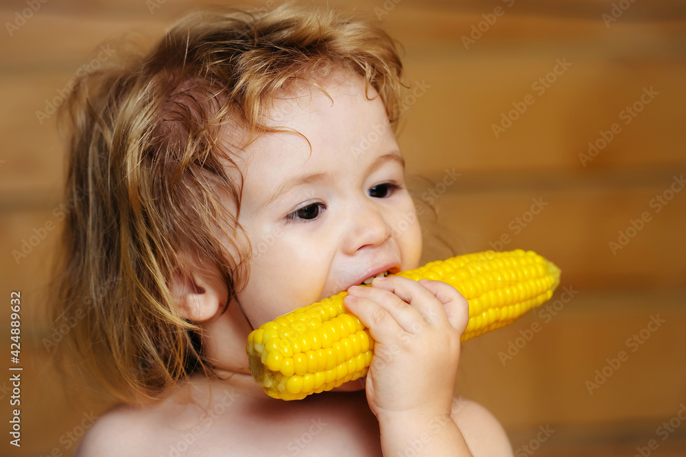 Baby eating yellow corn or maize with and funny face on wooden background. Baby eating yellow corn or maize with and funny face on wooden background.