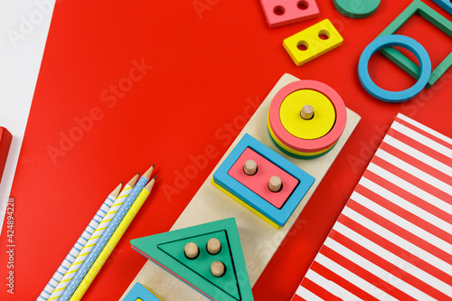Multicolored wooden blocks on red background. Trendy puzzle toys. Geometric shapes: square, circle, triangle, rectangle. Educational toys for kindergarten, preschool or daycare. Back to school 
