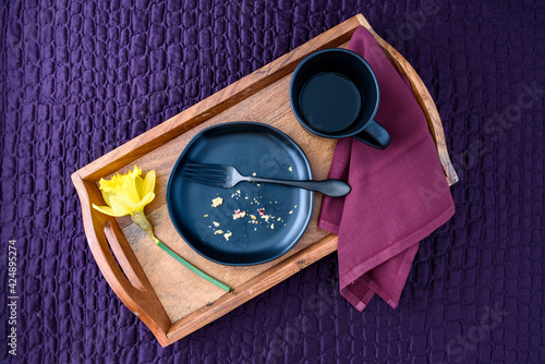 Breakfast in bed, black plate with scone crumbs and wood tray on a purple bedspread
