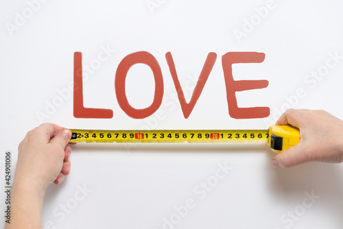 Hands measuring with measuring tape word LOVE on wall. Abstract concept.