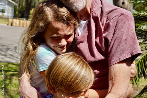 A grandfather is reunited with his granddaughter and grandson after a year apart due to the COVID pandemic. The children run to him and they hug. photo