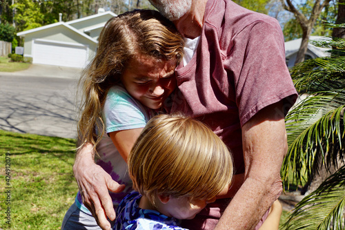 A grandfather is reunited with his granddaughter and grandson after a year apart due to the COVID pandemic. The children run to him and they hug.