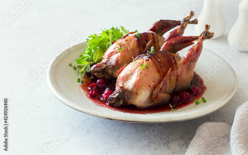 Oven baked quails served with berry sauce on stone plate close up