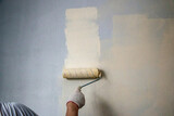 mans hand in cloth glove with paint roller applies fresh paint and primer to wall surface. process of applying water-based paint and primer with paint roller on surface for  interior design of room.