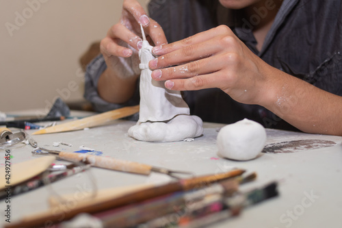 artisan hands molding a sculpture in clay and molding paste, on a table with several molding tools and brushes