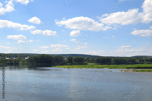 Quiet river in Siberia. Small ripples in the water. Beautiful cloudless warm summer day. Forest with houses in the background