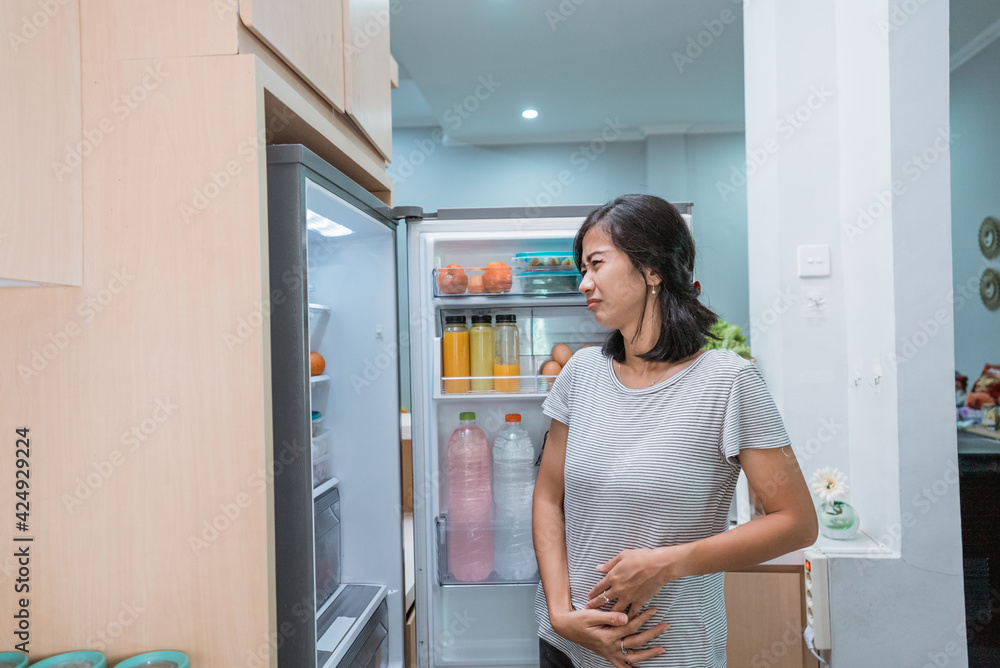 portrait of starving young asian woman hold her belly while open the fridge door looking for something to eat portrait of starving young asian woman hold her belly while open the fridge door looking for something to eat