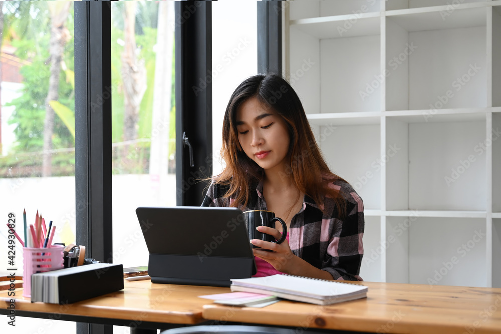 Young woman creative designer holding coffee cup and working on computer tablet at office. Young woman creative designer holding coffee cup and working on computer tablet at office.