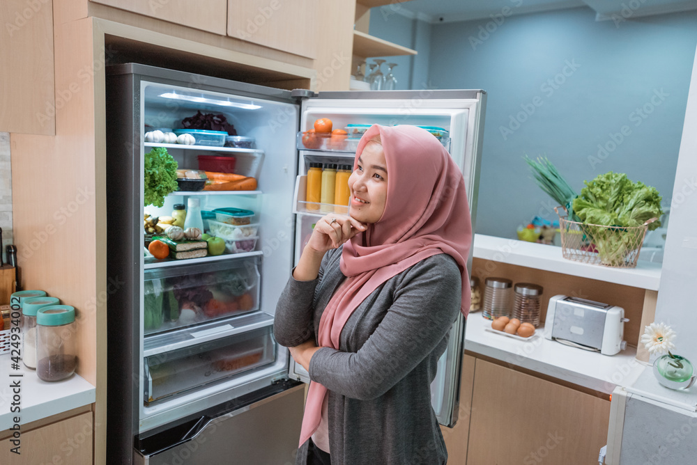 muslim asian woman thinking while open the refrigerator door before cooking in the kitchen muslim asian woman thinking while open the refrigerator door before cooking in the kitchen