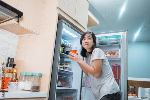 asian woman cheat diet and drinking sweet drink taking from the refrigerator