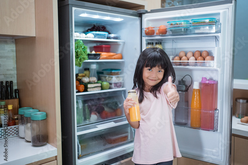 happy young asian girl open fridge door drinking a bottle of juice