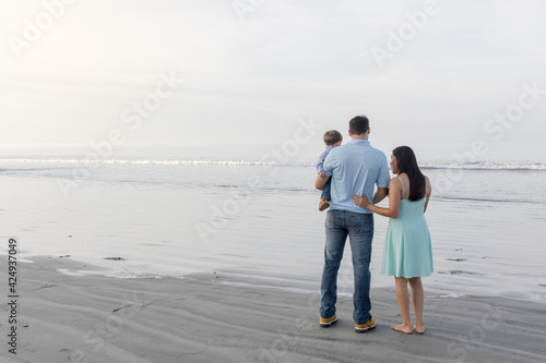 Family of three standing on the beach by the ocean looking out towards the horizon, Coronado California