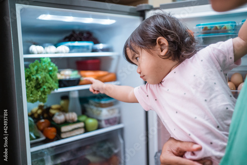 toddler asking for some food inside the refrigerator with father