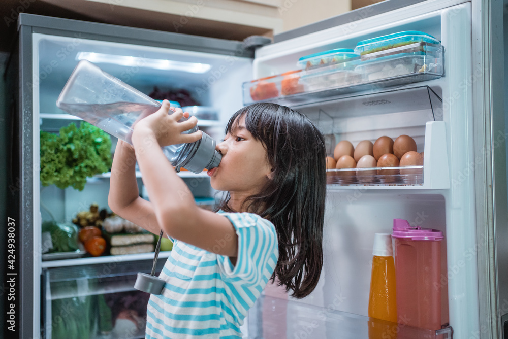 thirsty happy young asian girl open fridge door drinking a bottle of water thirsty happy young asian girl open fridge door drinking a bottle of water