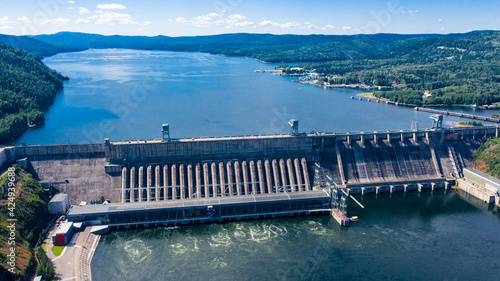 Aerial photography. Bird's eye view of the Krasnoyarsk Hydroelectric Power Plant. A powerful dam blocking the Yenisei River. Depicted on a 10 ruble bill of Russia. Mountains and green mountain taiga