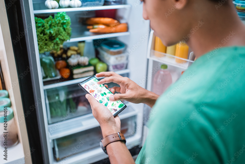 close up of hand ordering groceries online via mobile phone apps with open fridge background