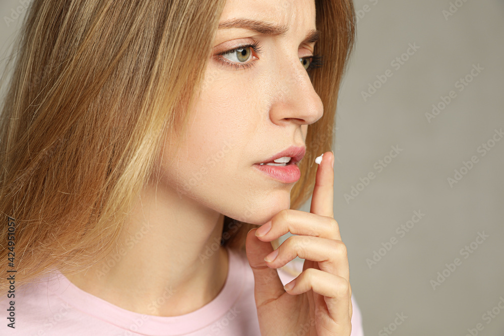 Woman with herpes applying cream onto lip against light grey background Woman with herpes applying cream onto lip against light grey background