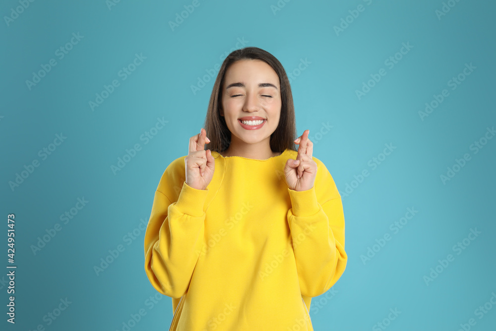 Woman with crossed fingers on light blue background. Superstition concept Woman with crossed fingers on light blue background. Superstition concept
