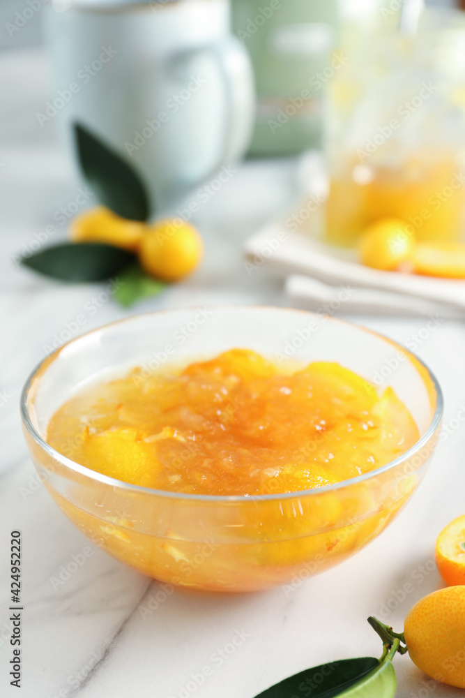Delicious kumquat jam in glass bowl on white marble table Delicious kumquat jam in glass bowl on white marble table