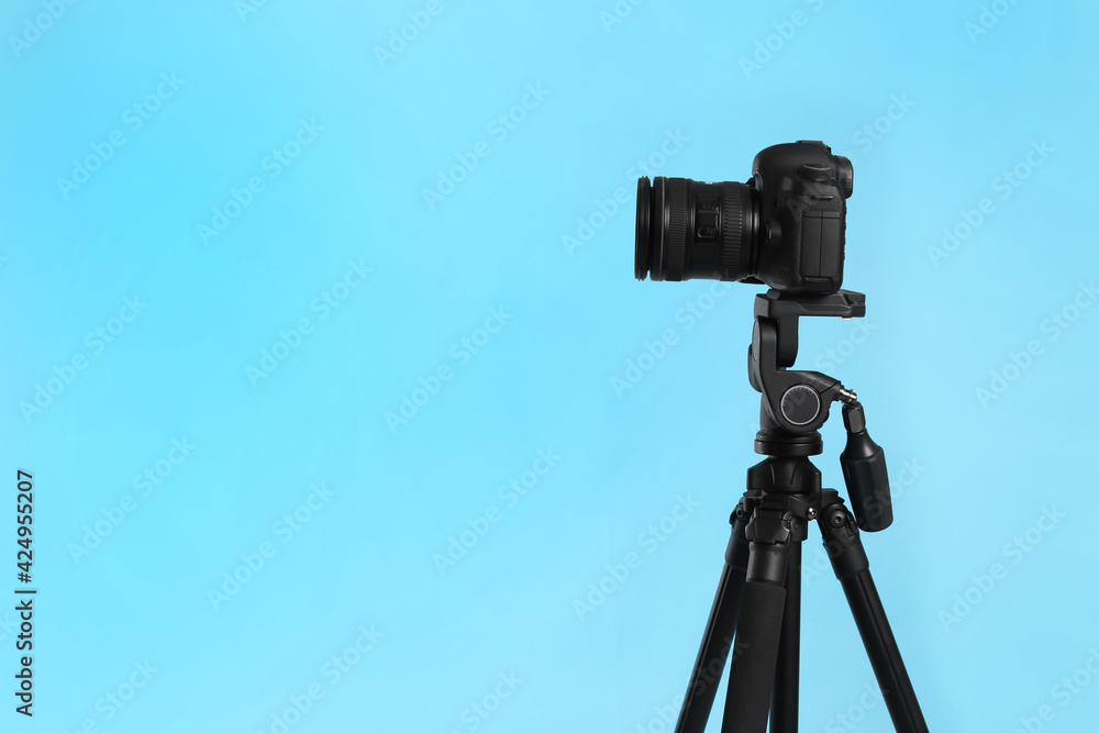 Modern tripod with professional camera on light blue background. Space for text Modern tripod with professional camera on light blue background. Space for text