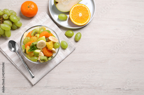 Delicious fresh fruit salad in bowl on white wooden table, flat lay. Space for text