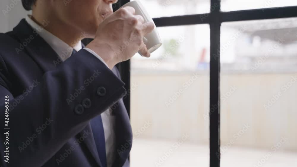 Businessman wearing glasses in a good mood smile thinking with holding coffee cup, man standing near window looking out the windows. Businessman wearing glasses in a good mood smile thinking with holding coffee cup, man standing near window looking out the windows.