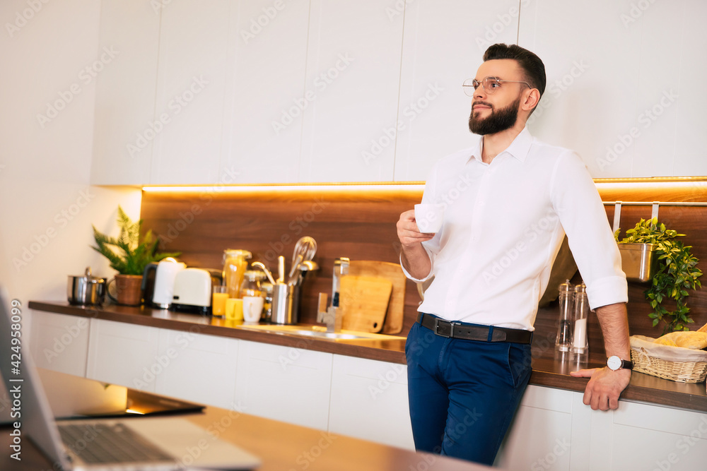 Relaxed bearded confident businessman in smart casual wear drinks smells coffee and thoughtful at domestic kitchen Relaxed bearded confident businessman in smart casual wear drinks smells coffee and thoughtful at domestic kitchen