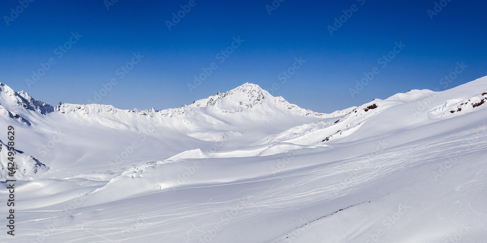 Snow covered Ullukambashi mount and Hotu-Tau plateau in sunny winter day, view from Elbrus ski slope in Kabardino-Balkaria, Russia. Snow covered Ullukambashi mount and Hotu-Tau plateau in sunny winter day, view from Elbrus ski slope in Kabardino-Balkaria, Russia.