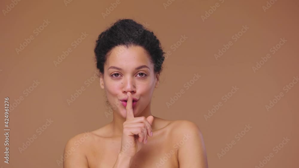 Beauty portrait of young African American woman coquettishly looking at camera and showing hush gesture, secret. Black female on brown studio background. Slow motion ready, 4K at 59.94fps. Beauty portrait of young African American woman coquettishly looking at camera and showing hush gesture, secret. Black female on brown studio background. Slow motion ready, 4K at 59.94fps.