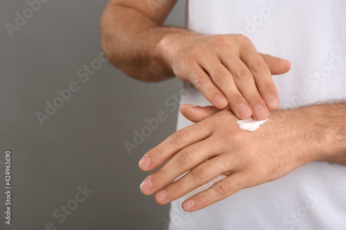 Man applying cream onto hand on grey background, closeup