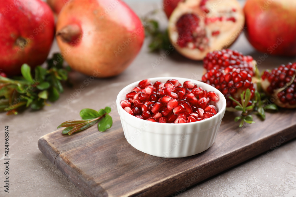Delicious ripe pomegranate kernels in bowl on grey table Delicious ripe pomegranate kernels in bowl on grey table