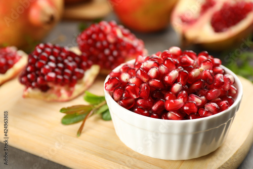 Delicious ripe pomegranate kernels in bowl on wooden board, closeup. Space for text