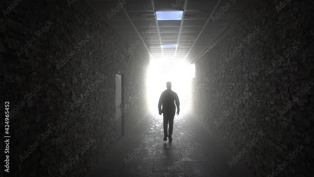 Light at the end of the tunnel. The dark silhouette of a man moves. Corridor with bright light. Stone walls and floor. Shadow of a man on the floor. Mysticism. Light at the end of the tunnel. The dark silhouette of a man moves. Corridor with bright light. Stone walls and floor. Shadow of a man on the floor. Mysticism.
