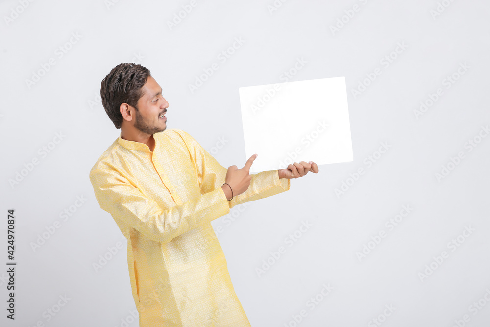 Indian man holding white board, promoting offers on festival season while wearing traditional cloths, standing over white background. Indian man holding white board, promoting offers on festival season while wearing traditional cloths, standing over white background.