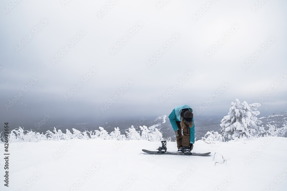 Snowboarder female putting on one leg in snowboard preparing to slide down slope in winter ski resort