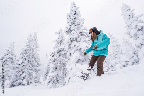 Snowboarder female riding through winter snow cowered spruce forest on snowboard. Powder Day. Freeride on winter holiday