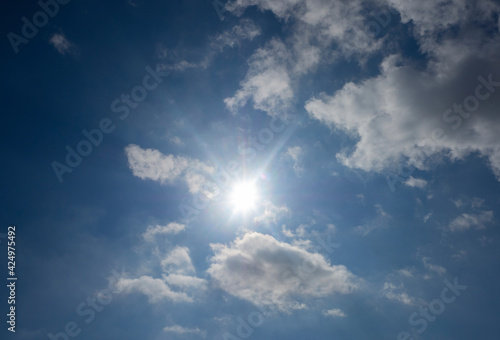 The sun with rays in a blue sky with white cirrus clouds.
