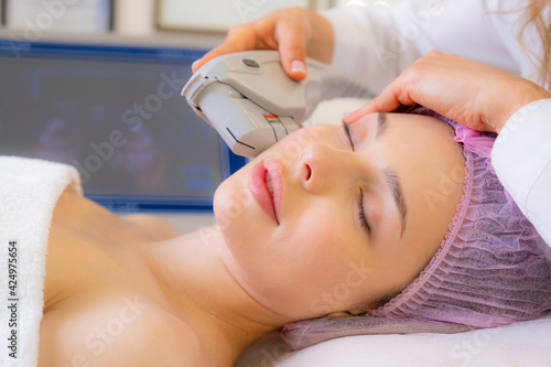 Woman in a spa salon on cosmetic procedures for facial care. Cosmetologist making a woman a therapeutic laser processing on a face. Beautician makes laser procedures on a female face.