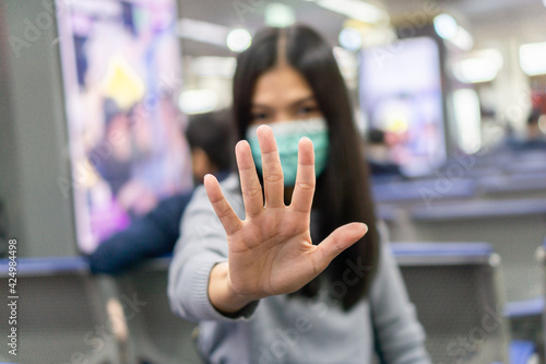 Asian woman wearing a surgical mask to protect against coronavirus, Lady sitting at Bangkok International Airport and show stop hands gesture.