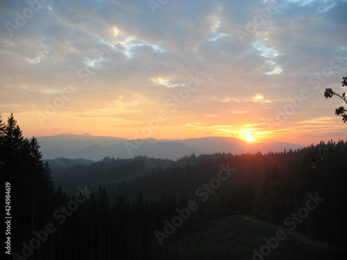 Sunset in the mountains, sky with gray-orange clouds, yellow sun and mountain ranges on the horizon, Carpathian Mountains