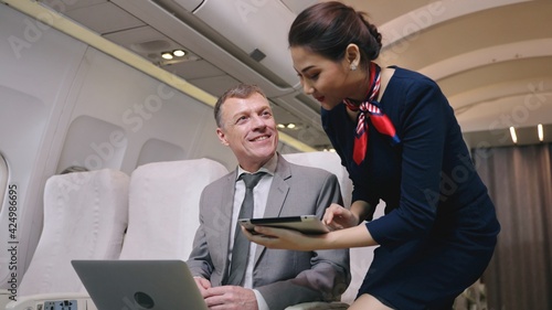 Airplane Stewardess Sending Digital tablet choose food order service on the plane flight, Business class. Flight Attendant Shows Tablet Computer with Menu to Caucasian Male Passenger. They're Inflight