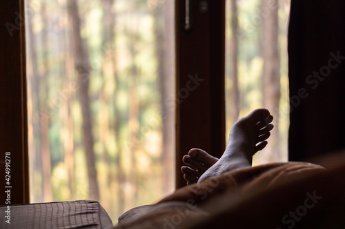 Man's feet on the bed, a view of the pine forest of Thailand.