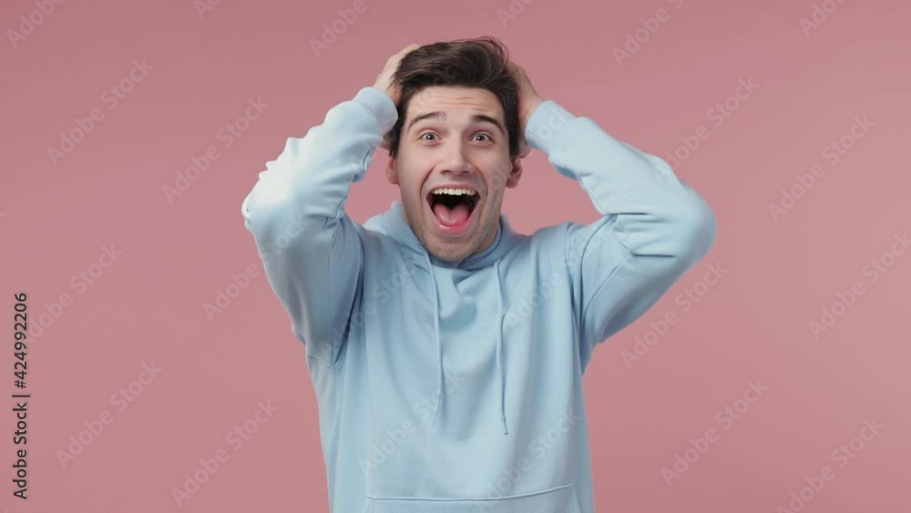 Joyful surprised excited overjoyed happy brunet young man 20s wears blue streetwear hoodie say wow what spreading hands doing winner gesture scream isolated on pastel pink background studio portrait Joyful surprised excited overjoyed happy brunet young man 20s wears blue streetwear hoodie say wow what spreading hands doing winner gesture scream isolated on pastel pink background studio portrait