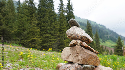 Pile of stones in the mountains - tour. The atmosphere of the forest, green grass, coniferous trees, flowers, stones. The sky is covered with dark clouds. © SergeyPanikhin