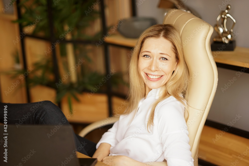 A beautiful smiling businesswoman in a white shirt sits on the chair at the office. Confident woman concept A beautiful smiling businesswoman in a white shirt sits on the chair at the office. Confident woman concept